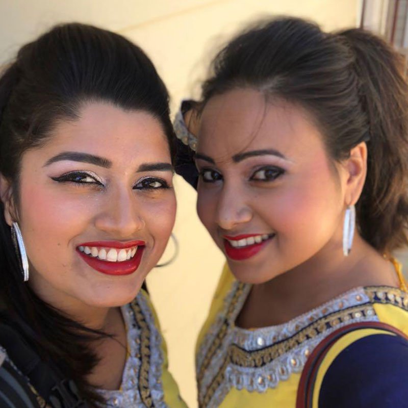 Two women in yellow embroidered festive wear with winged liner, red lipstick, and shaped brows.